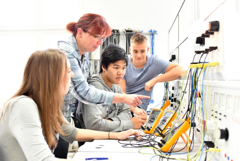 Unterricht in Elektrotechnik bei der Berufsausbildung - Gruppe von Auszubildenten und einer Lehrerin // Teaching in Electrical Engineering - group of trainees and a teacher